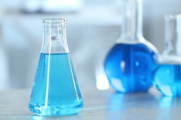 Frasco cónico com líquido azul claro sobre mesa em laboratório. Espaço para texto — Fotografia de Stock