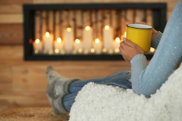 Mujer con taza de bebida caliente cerca de chimenea decorativa en el interior, primer plano. Ambiente de invierno — Foto de Stock