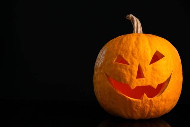 Siyah arka planda korkunç suratlı bir balkabağı. Cadılar Bayramı geleneği