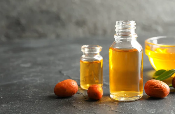 Jojoba oil and seeds on dark grey table