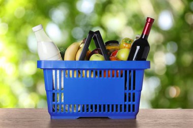 Bulanık arka planda ahşap masada sebze ürünleri olan alışveriş sepeti.