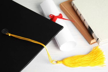 Mezuniyet şapkası ve öğrenci diploması beyaz ahşap masada, üst tarafta.