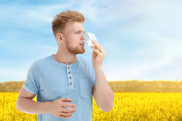 Молодой человек, страдающий аллергией и цветущим полем на заднем плане — стоковое фото