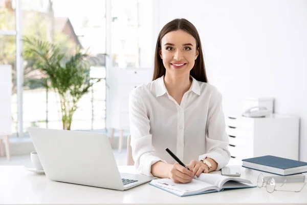 Młoda bizneswoman pisząca w notatniku podczas korzystania z laptopa przy stole w biurze — Zdjęcie stockowe