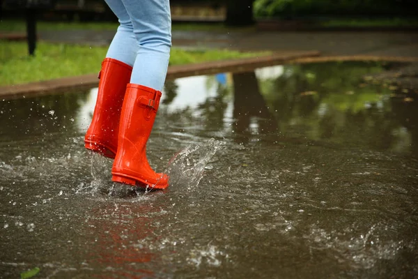 赤いゴムのブーツを持つ女性が水たまりに飛び込み、クローズアップ。雨天 — ストック写真