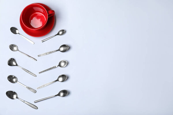 Composition with new metal spoons and red cup on white background, top view