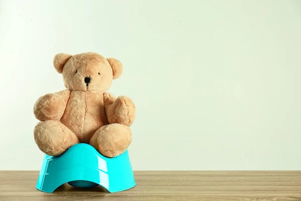 Teddy bear with blue potty on wooden table against light background, space for text. Toilet training — Stock Photo, Image