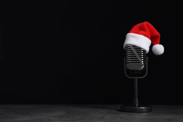 Micrófono con sombrero de Santa sobre mesa de piedra gris sobre fondo negro, espacio para texto. Música navideña — Foto de Stock