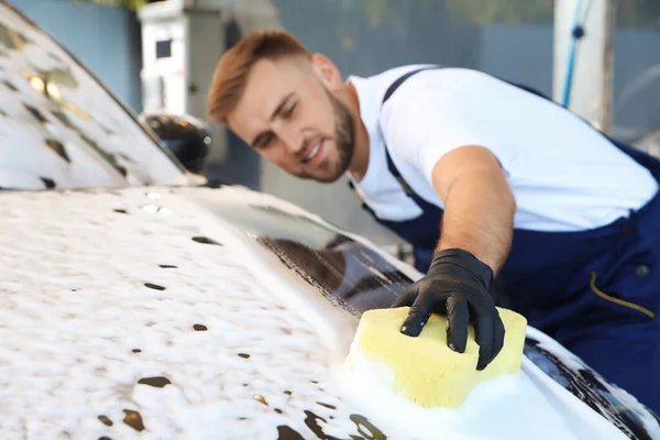 Молодой рабочий чистит автомобиль с губкой на автомойке — стоковое фото
