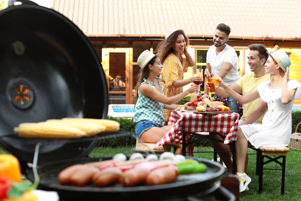 Gruppo di amici alla festa barbecue all'aperto. Vista offuscata della griglia con salsicce e verdure — Foto Stock