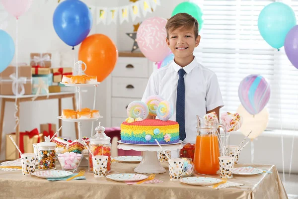 Boldog fiú az asztalnál édességekkel a szülinapi bulira díszített szobában — Stock Fotó