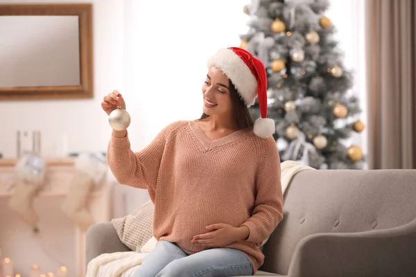 Šťastná těhotná žena s vánoční koulí v obýváku. Očekává se dítě — Stock fotografie
