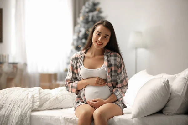 Mujer embarazada feliz en la cama en la habitación decorada para Navidad. Esperando un bebé — Foto de Stock