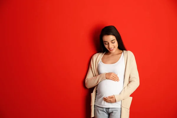 Mujer embarazada feliz sobre fondo rojo, espacio para el texto. Esperando un bebé — Foto de Stock