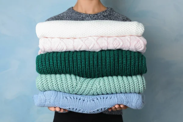 Woman holding stack of warm clothes on light blue background, closeup. Autumn season — Stock Photo, Image