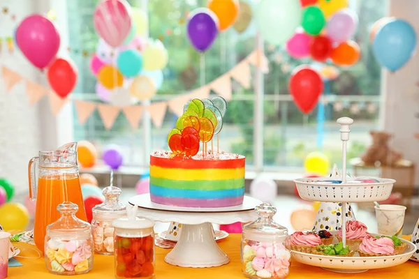 Bright birthday cake and other treats on table in decorated room — Stock Photo, Image