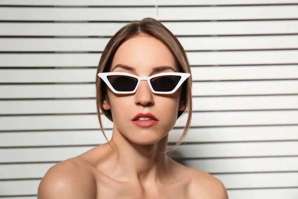 Mujer joven con gafas de sol elegantes contra persianas — Foto de Stock