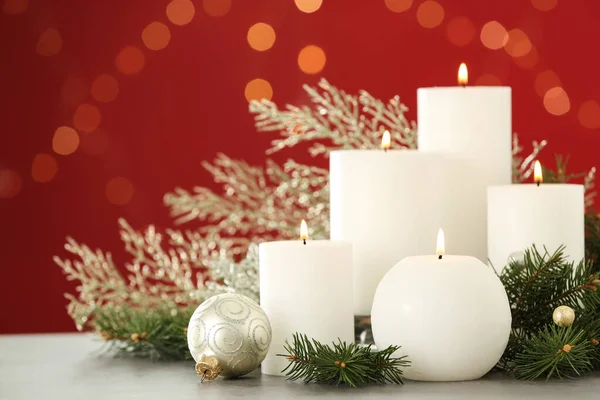 Queimando velas brancas e decoração de Natal na mesa contra fundo vermelho com efeito bokeh — Fotografia de Stock