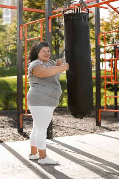 美しいです太りすぎ女性キックヘビーバッグ上のスポーツグラウンド — ストック写真