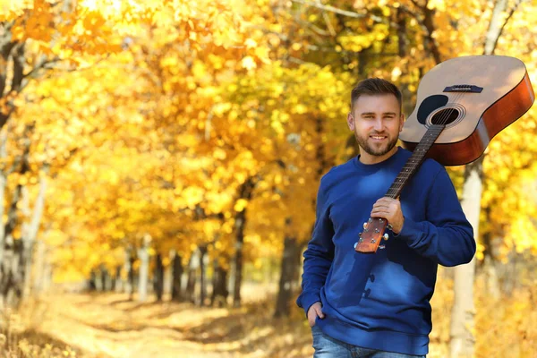 Молодий чоловік з акустичною гітарою в осінньому парку — стокове фото