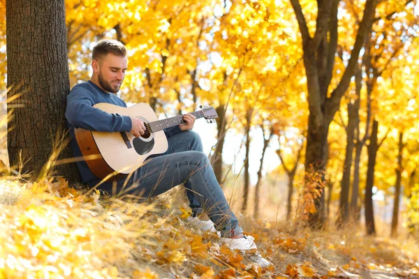 Jeune homme jouant de la guitare à l'automne parc — Photo