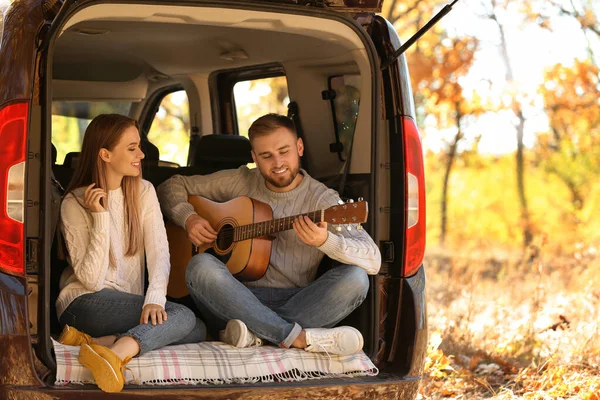 Coppia giovane con chitarra seduta nel bagagliaio dell'auto all'aperto — Foto Stock