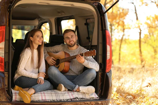 Unga par med gitarr sitter i öppen bil bagageutrymme utomhus — Stockfoto