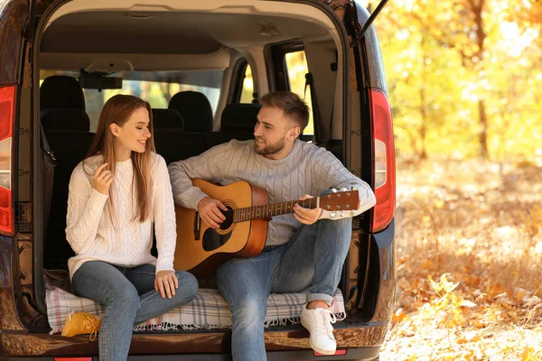 Coppia giovane con chitarra seduta nel bagagliaio dell'auto all'aperto — Foto Stock