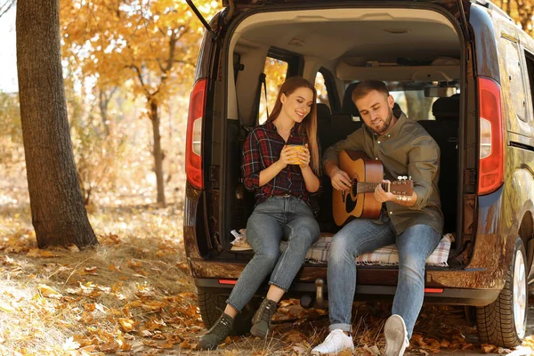 Coppia giovane con chitarra seduta nel bagagliaio dell'auto all'aperto — Foto Stock