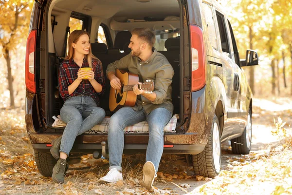 Pareja joven con guitarra sentada en el maletero abierto al aire libre — Foto de Stock