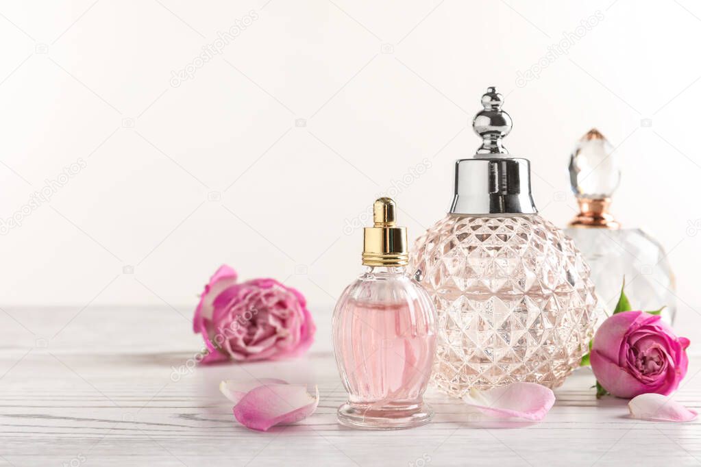 Different bottles of perfume and flowers on light background, space for text