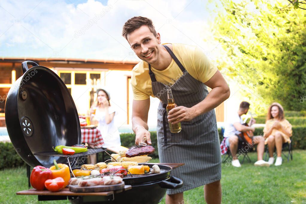 Young man with beer cooking on barbecue grill outdoors