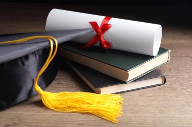 Mezuniyet şapkası, kitaplar ve ahşap masada öğrenci diploması.