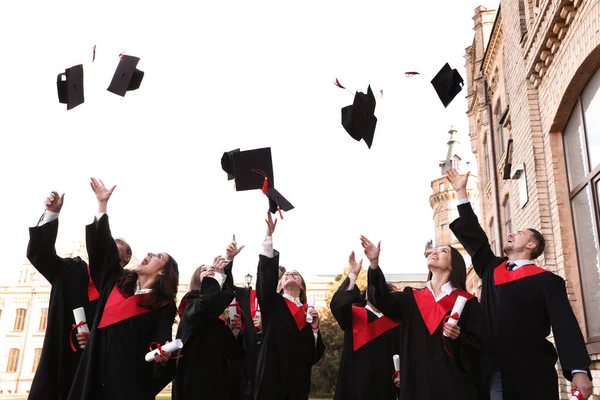 Щасливі студенти з дипломами кидають випускні капелюхи на відкритому повітрі — стокове фото