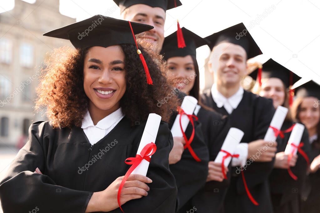 Happy students with diplomas outdoors. Graduation ceremony