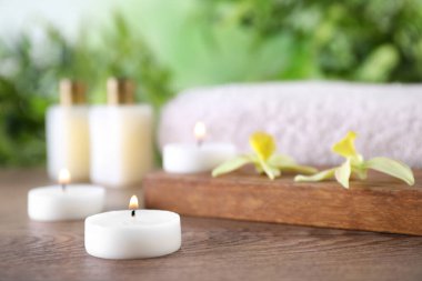 Ahşap masanın üzerinde yanan mumlar ve çiçekler olan kompozisyon bulanık arka planda, yazı için yer var. Spa konsepti
