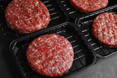 Gri masada hamburgerler için çiğ et bulunan plastik kaplar.