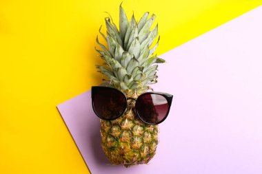 Pineapple with stylish sunglasses on color background, top view