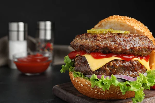 Pyszny burger z kotletami mięsnymi na czarnym stole, zbliżenie. Miejsce na tekst — Zdjęcie stockowe