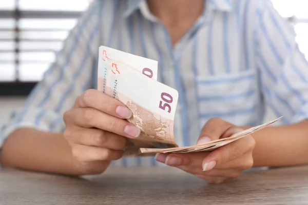 Женщина с банкнотами евро за деревянным столом в помещении, крупным планом — стоковое фото