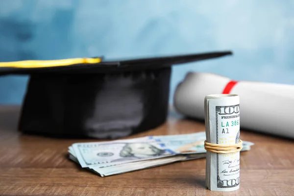 Dollar banknotes and student graduation hat on wooden table against blue background. Tuition fees concept — Stock Photo, Image