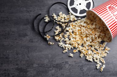 Bir kova taze patlamış mısır ve film makarası gri taş masada, düzlük ve yazı için yer var. Sinema atıştırması