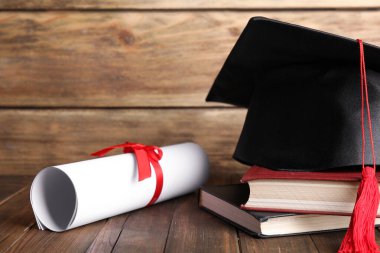 Mezuniyet şapkası, kitaplar ve ahşap masada öğrenci diploması.