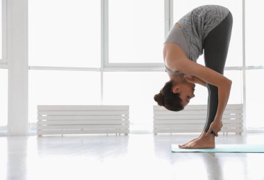 Genç bir kadın yoga stüdyosunda Asana 'yı öne doğru eğip pratik yapıyor. Uttanasana pozu