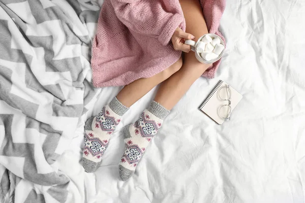 Woman with cocoa wearing knitted socks on white fabric, top view. warm clothes — ストック写真