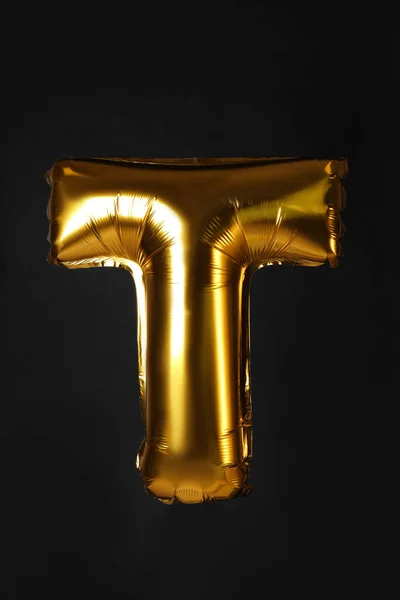 Golden letter T balloon on black background — ストック写真