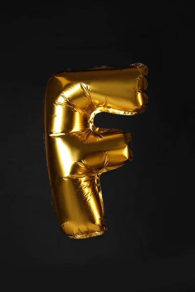 Goldene Buchstaben f Ballon auf schwarzem Hintergrund — Stockfoto