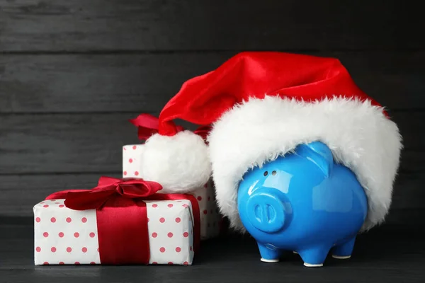 Sparschwein mit Weihnachtsmütze und Geschenkschachteln auf schwarzem Holztisch — Stockfoto