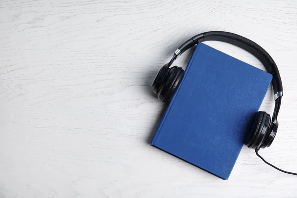 Headphones modernos com livro de capa dura sobre fundo de madeira branco, vista superior. Espaço para texto — Fotografia de Stock