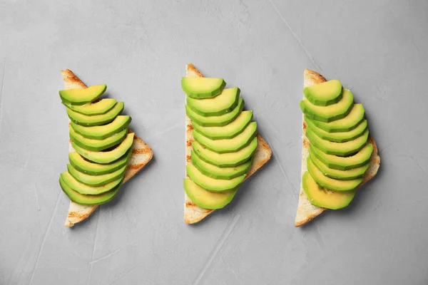 Tasty toasts with avocado on light grey table, flat lay — Stockfoto